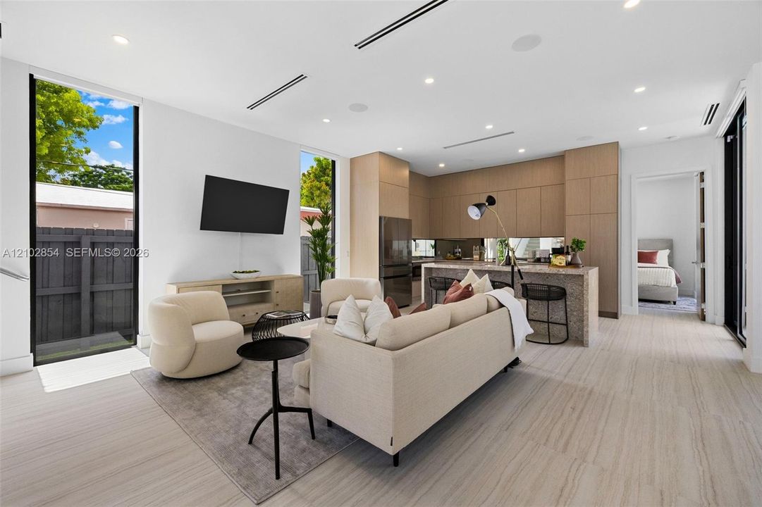 Open-concept interior featuring wood-finish flooring, floor-to-ceiling windows, recessed lighting, and kitchen cabinetry with a light wood finish