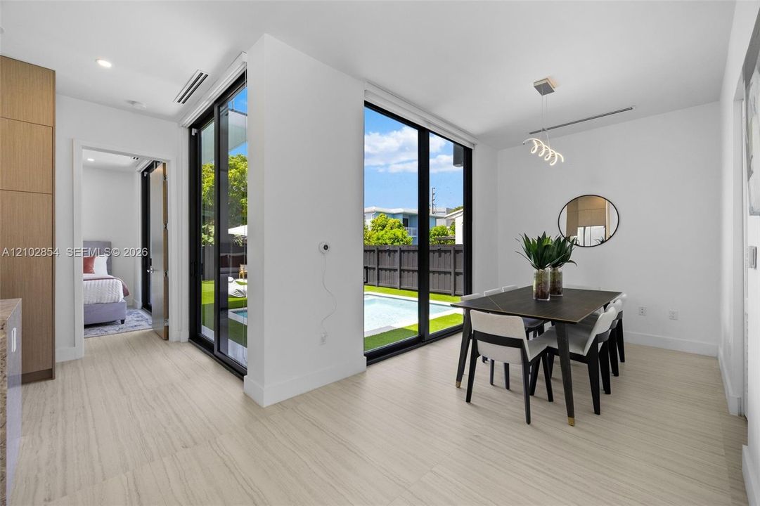 Floor-to-ceiling black-framed glass sliding doors, wood-finish tile flooring, recessed ceiling lighting, and custom wood-veneer cabinetry