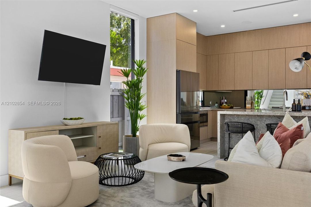 Modern kitchen featuring flat-panel wood-finish cabinetry, a stone-surfaced waterfall island, and reflective backsplash, illuminated by recessed lighting and vertical floor-to-ceiling windows