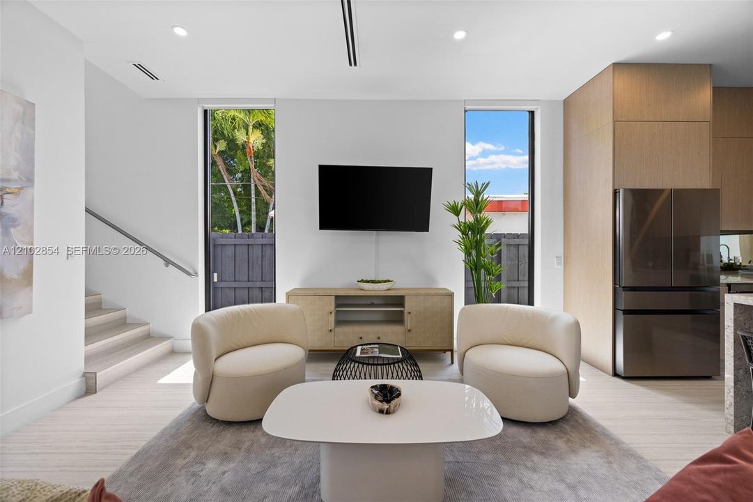 Open-concept interior featuring light wood-finish flooring, floor-to-ceiling windows, recessed ceiling lighting, and flat-panel wood cabinetry with an integrated stainless steel refrigerator