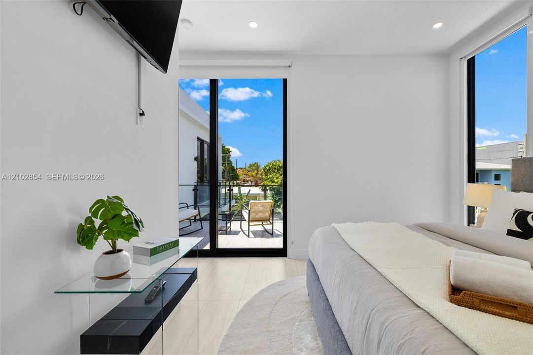 Light-filled room featuring large sliding glass doors, a glass-railed exterior balcony, neutral tile flooring, and recessed ceiling lighting