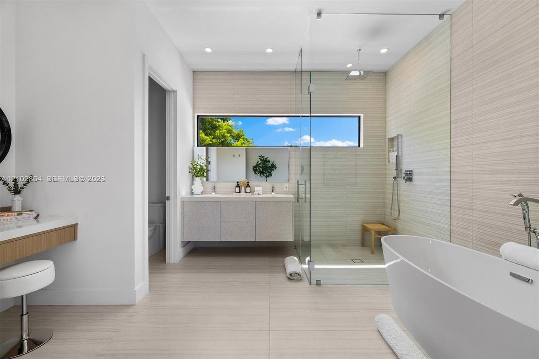 Floating vanity with integrated dual sinks, freestanding soaking tub, walk-in glass-enclosed shower, horizontal ribbon window, and floor-to-ceiling tile work