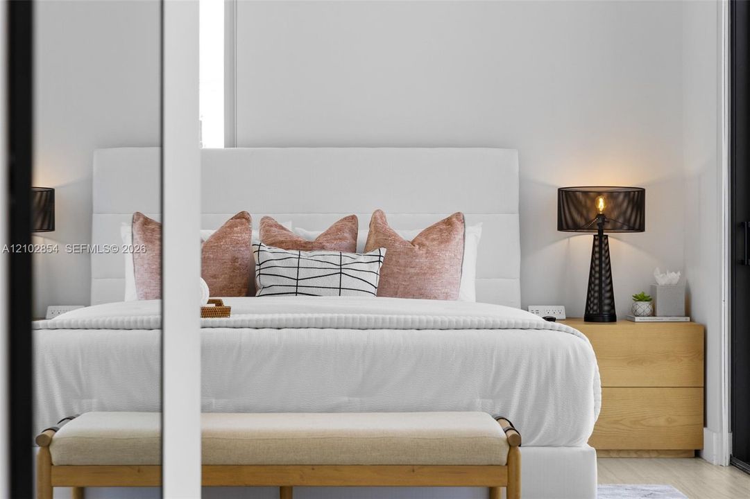 Minimalist sleeping area featuring neutral wall tones, a built-in upholstered headboard, and a mirrored closet panel