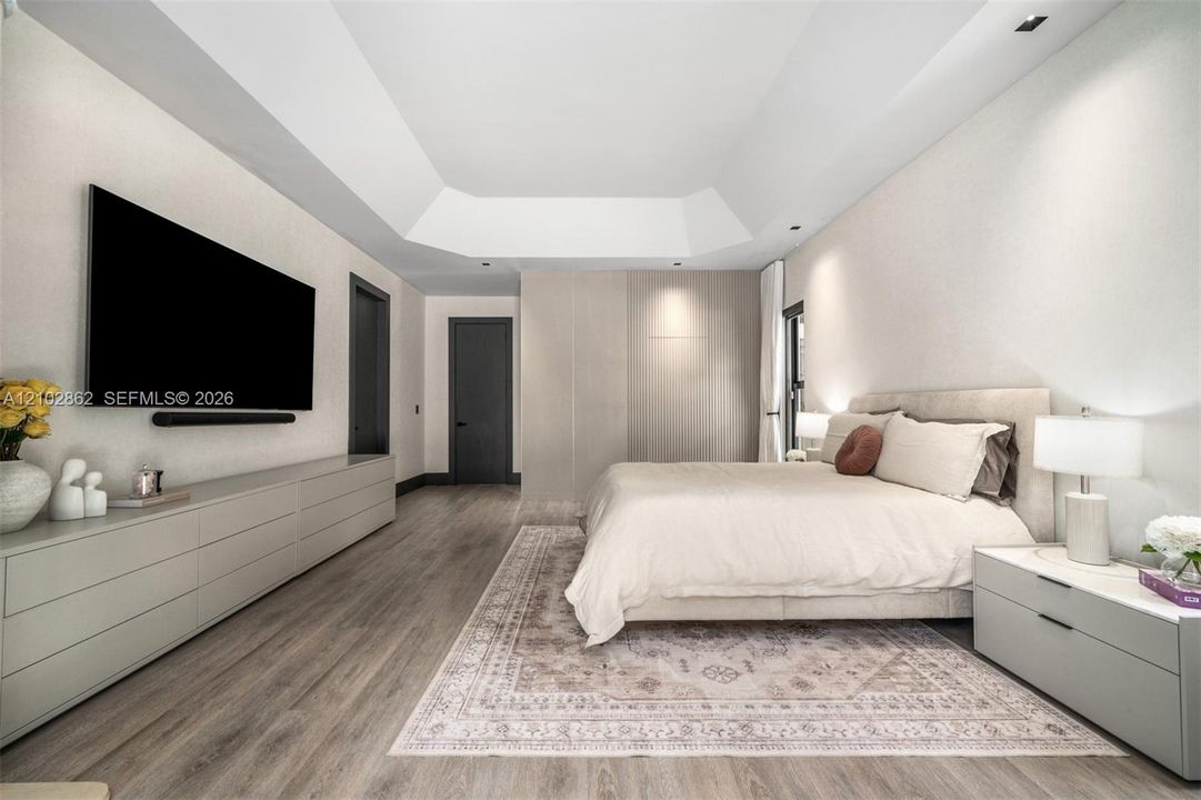 Tray ceiling with recessed lighting, integrated floor-to-ceiling cabinetry, wood-finish flooring, and minimalist flat-panel doors