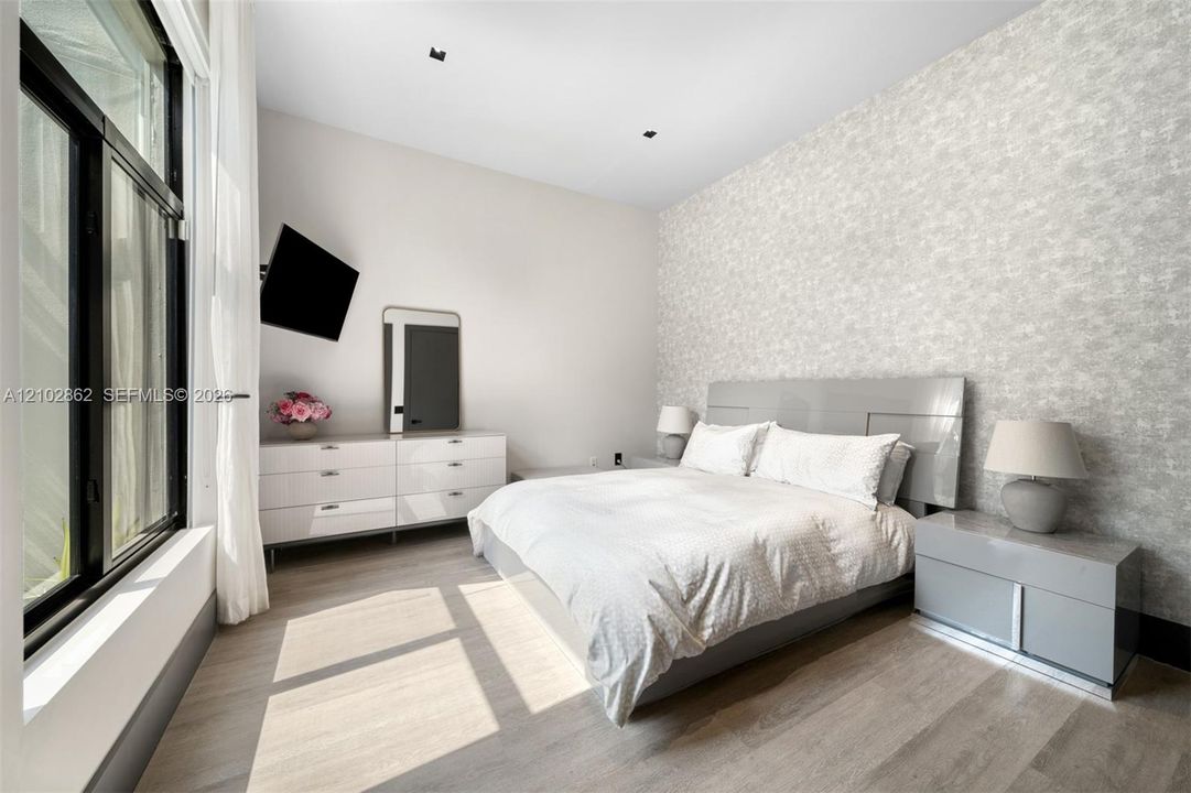 Bedroom featuring textured accent wall, floor-to-ceiling windows, recessed lighting, and wood-finish flooring