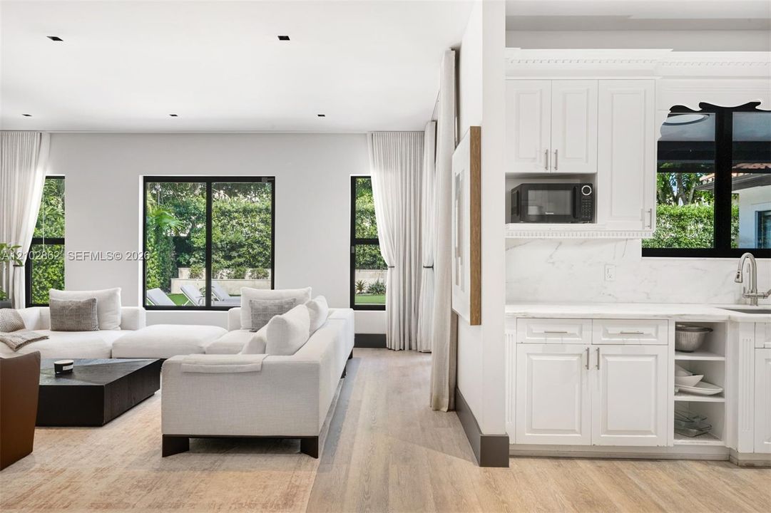 Open-concept interior featuring light wood-finish flooring, white shaker-style cabinetry, solid-surface countertops with stone-pattern veining, and multiple windows with black framing