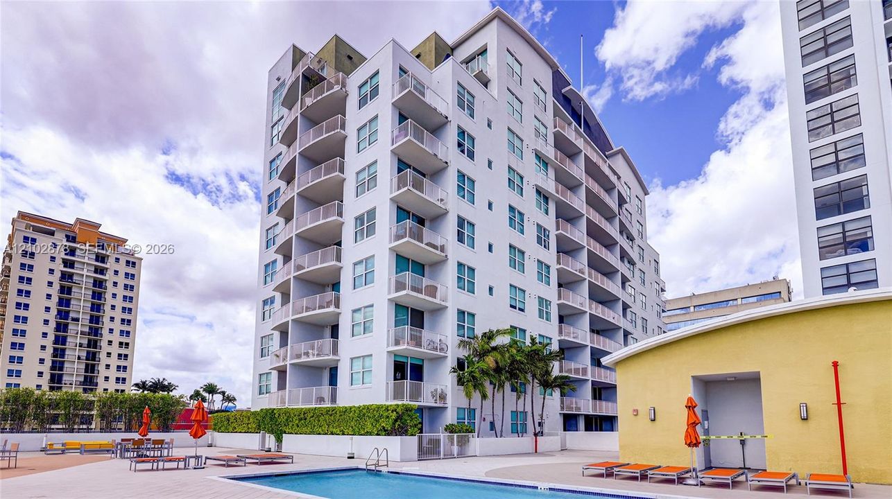Multi-story high-rise exterior featuring private balconies, integrated swimming pool, paved pool deck, and manicured perimeter landscaping