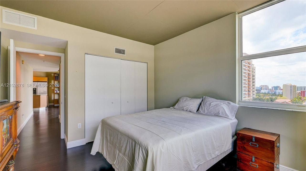 Bedroom featuring wood-finish flooring, a double-door closet, and large windows with exterior urban scenery