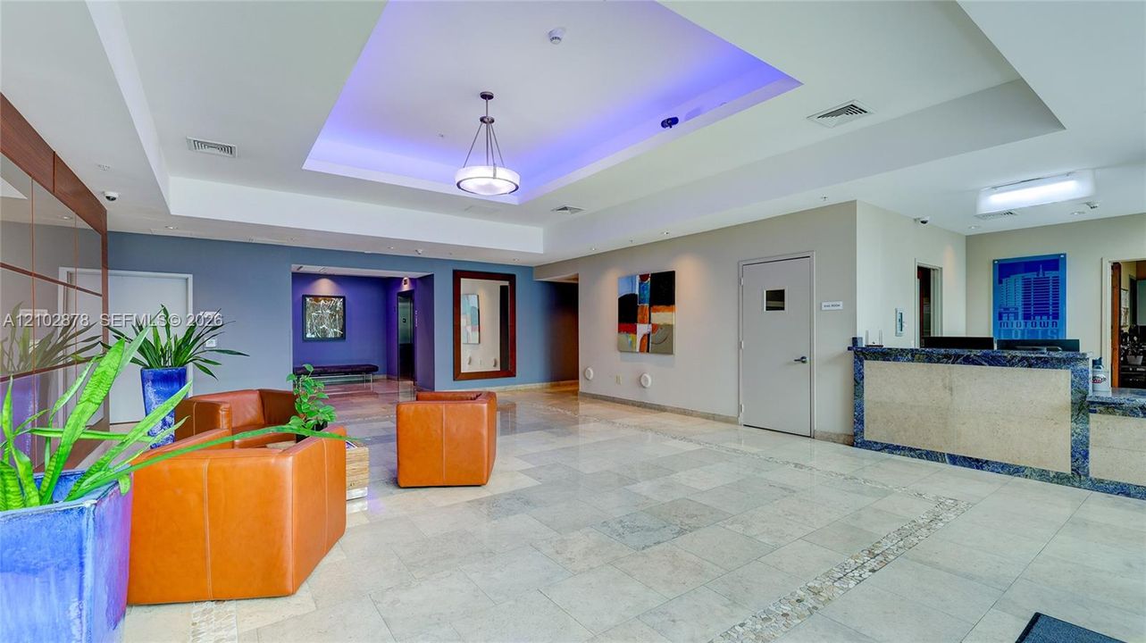 Lobby area featuring recessed ceiling detail with integrated lighting, polished stone flooring, and a stone-clad reception desk