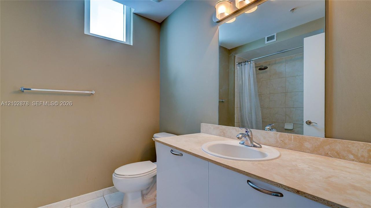 Bathroom featuring a stone-surface vanity with an integrated basin, white cabinetry, a large wall-mounted mirror, and a tub-shower combination with tile surround