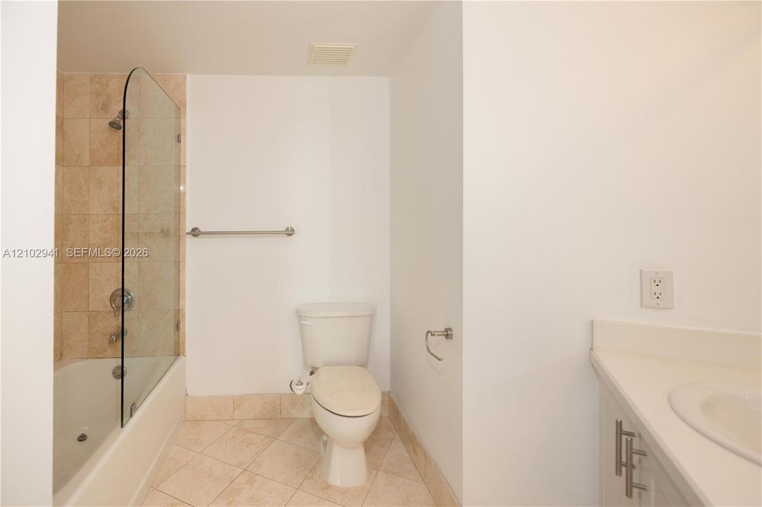 Bathroom featuring a tub-shower combination with a glass panel, stone-finish tile surround and flooring, and a solid-surface vanity countertop