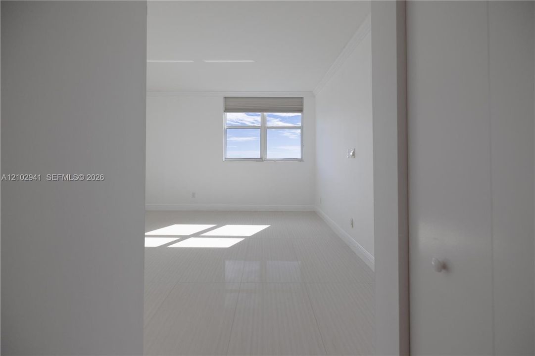 Neutral interior featuring large-format polished tile flooring, crisp white walls, crown molding, and a dual-pane window