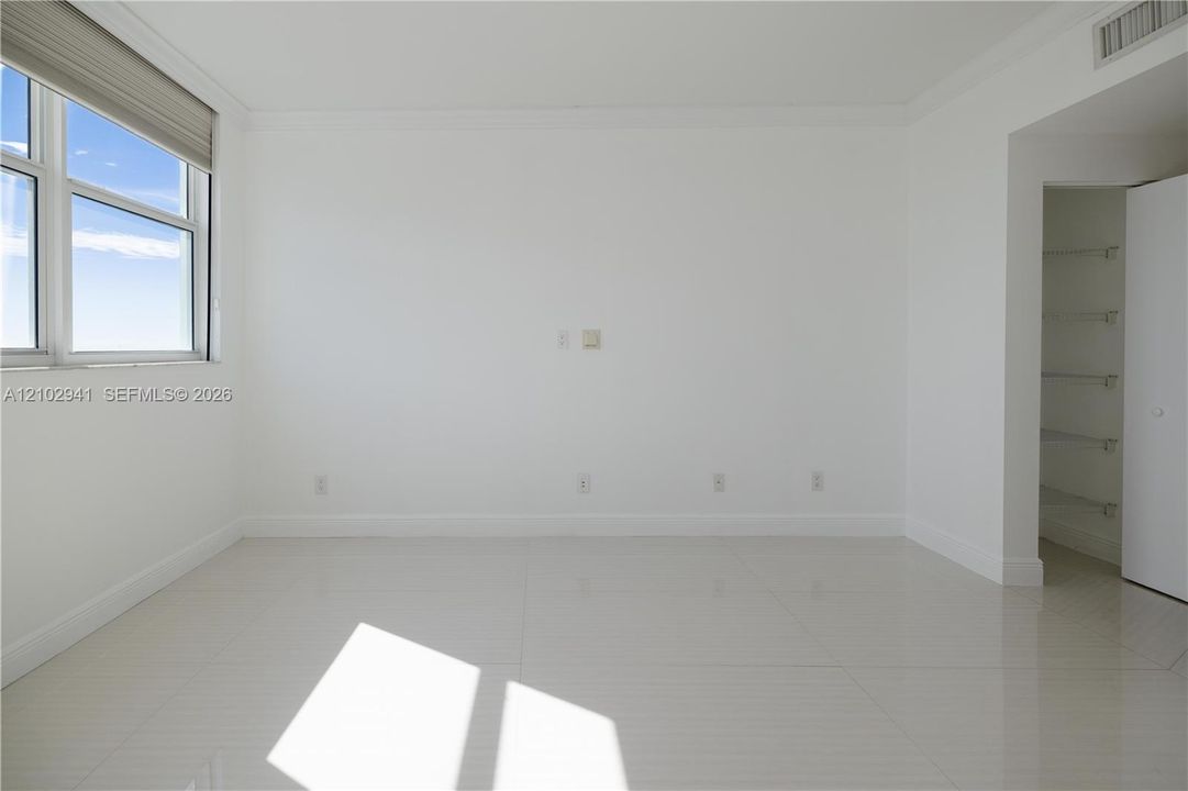 Neutral-toned large-format tile flooring, multi-pane window with retractable shade, and built-in closet with integrated shelving