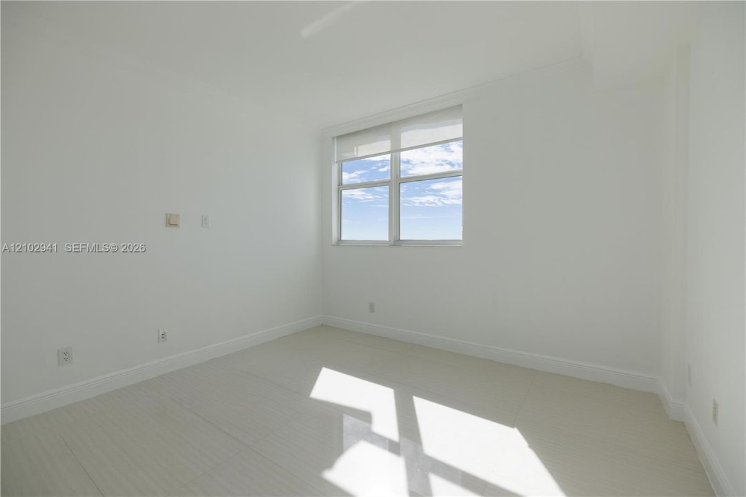 Neutral-toned interior space featuring light-colored tile flooring, smooth wall finishes, and a window with a retractable roller shade