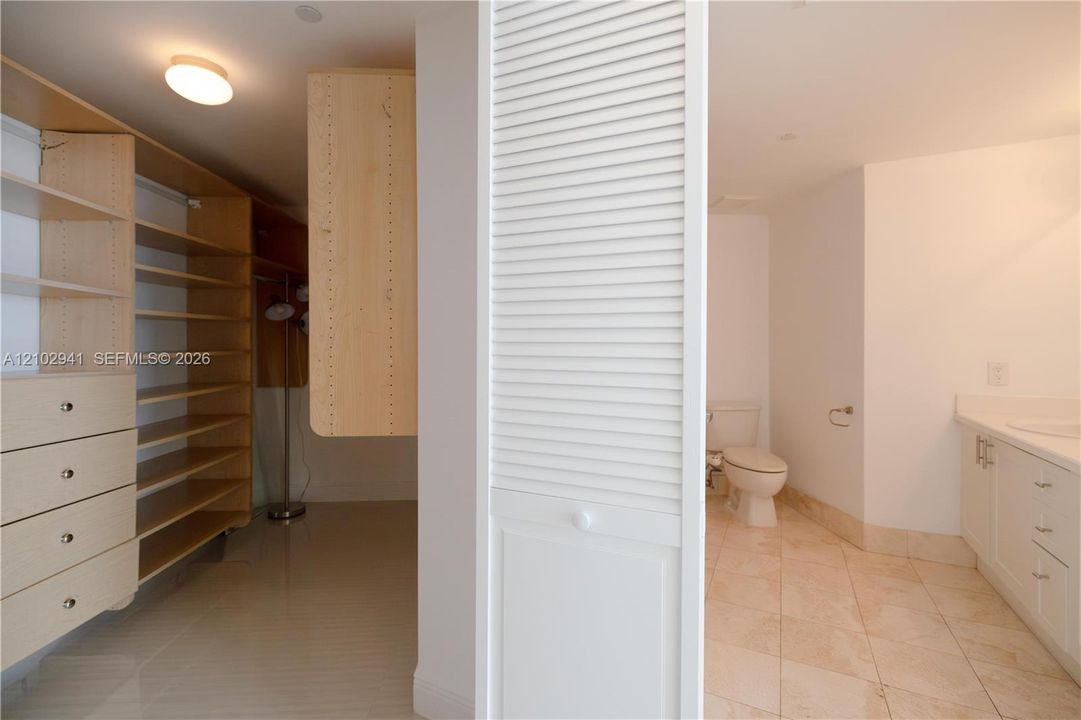 Custom built-in wood shelving and cabinetry with integrated drawers, light-toned tile flooring, white louvered closet doors, and a vanity featuring neutral cabinetry