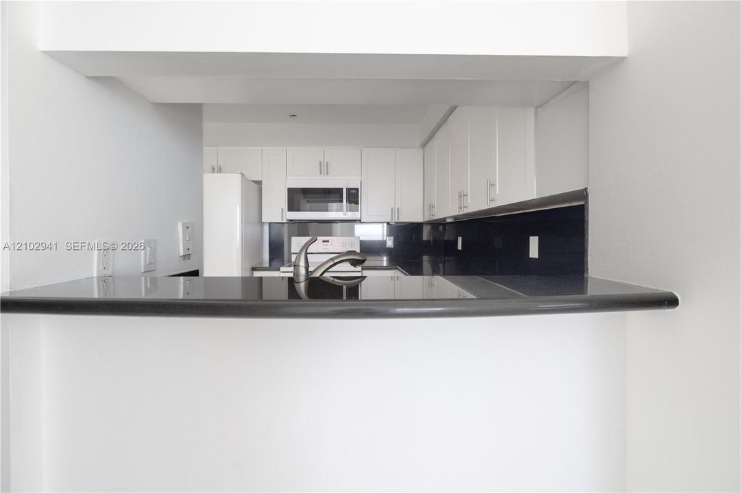 Kitchen featuring white cabinetry, contrasting dark countertops, a dark backsplash, a built-in microwave, and a stainless steel faucet