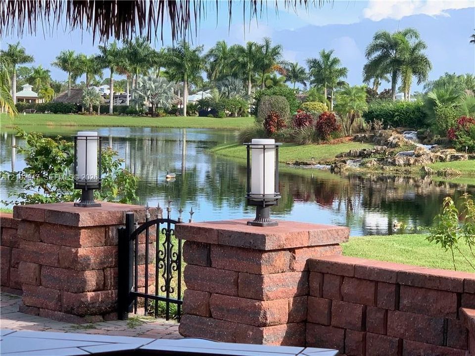 Patio area featuring a decorative brick retaining wall, wrought iron gate, custom pillar-mounted lighting, and a water feature backdrop