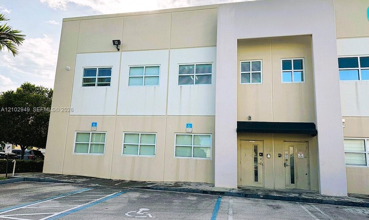 Two-story concrete exterior with multi-pane windows, recessed dual-entry doors, and dedicated paved parking