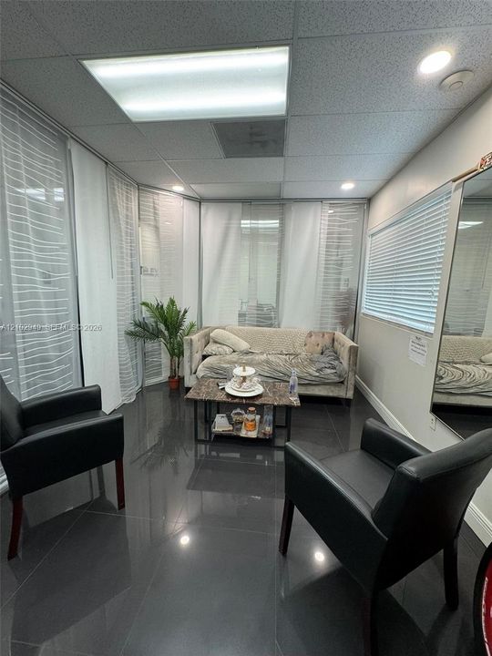Interior room featuring glossy tile flooring, wall-to-wall glass partitions with vertical blinds, a drop ceiling with recessed lighting, and a full-length wall mirror