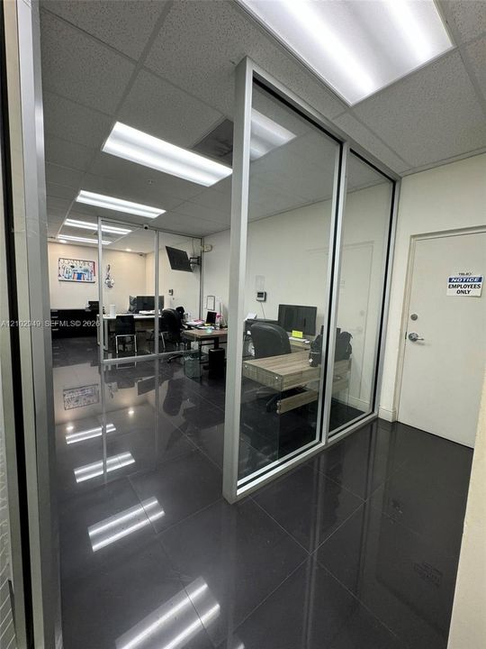 Polished black tile flooring, floor-to-ceiling glass panel walls with silver-tone aluminum frames, recessed fluorescent lighting, and dropped acoustical ceiling tiles