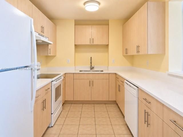 Kitchen featuring light-finish cabinetry, solid surface countertops, a stainless steel undermount sink with a gooseneck faucet, tile flooring, and white appliances