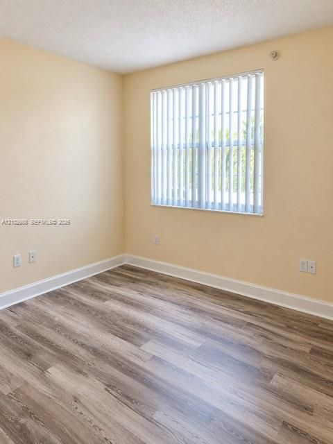 Room featuring neutral wall tones, wood-finish flooring, and a single window equipped with vertical blinds