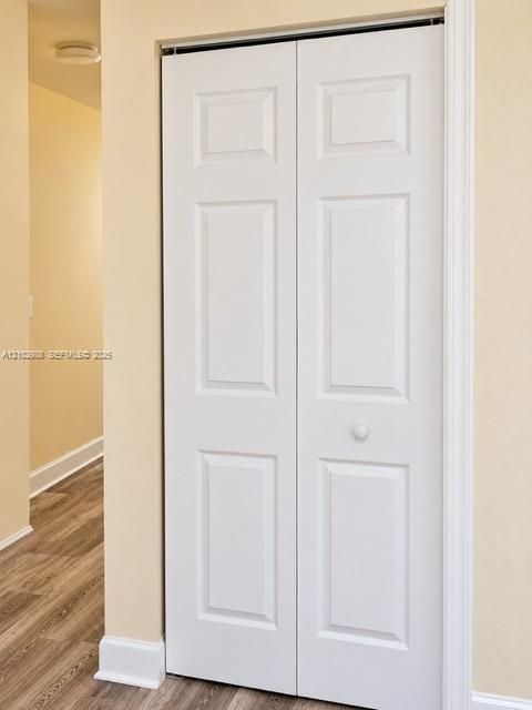 White six-panel bi-fold closet doors featuring a central knob, paired with wood-finish flooring