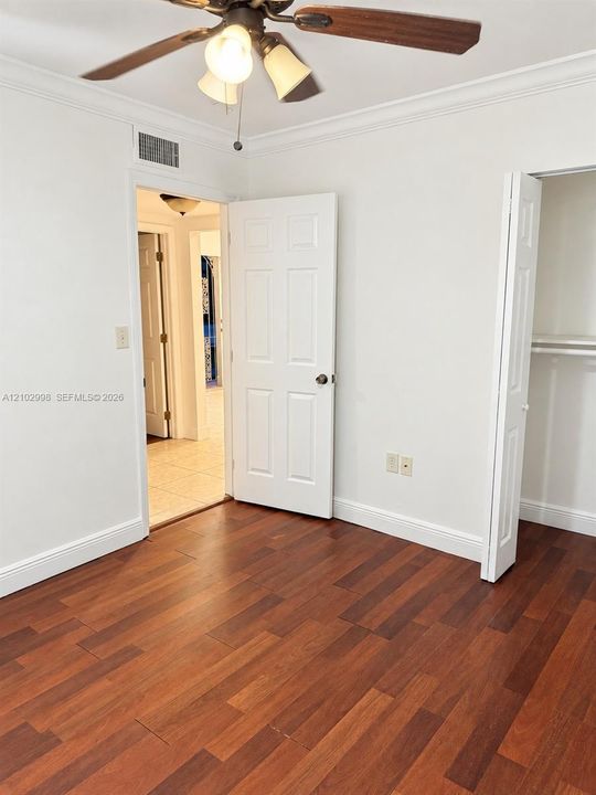Room featuring wood-finish flooring, crown molding, a ceiling fan with integrated lighting, and a closet with a bi-fold door