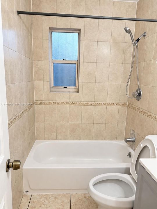 Bathroom featuring floor-to-ceiling neutral ceramic tile, decorative tile inlay, integrated shower and tub enclosure, handheld shower fixture, and privacy window