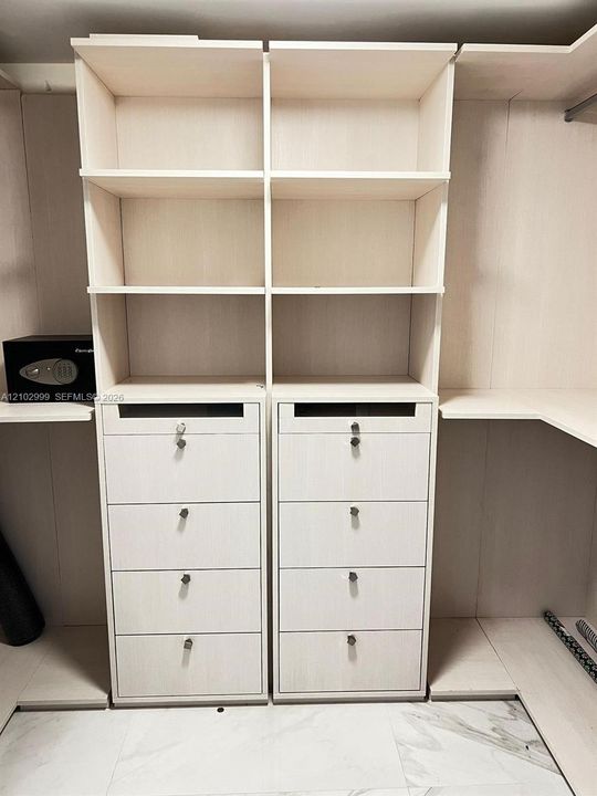 Custom closet organization featuring light-toned wood-finish cabinetry, built-in shelving, eight stackable drawers with locking mechanisms, and integrated hanging rods