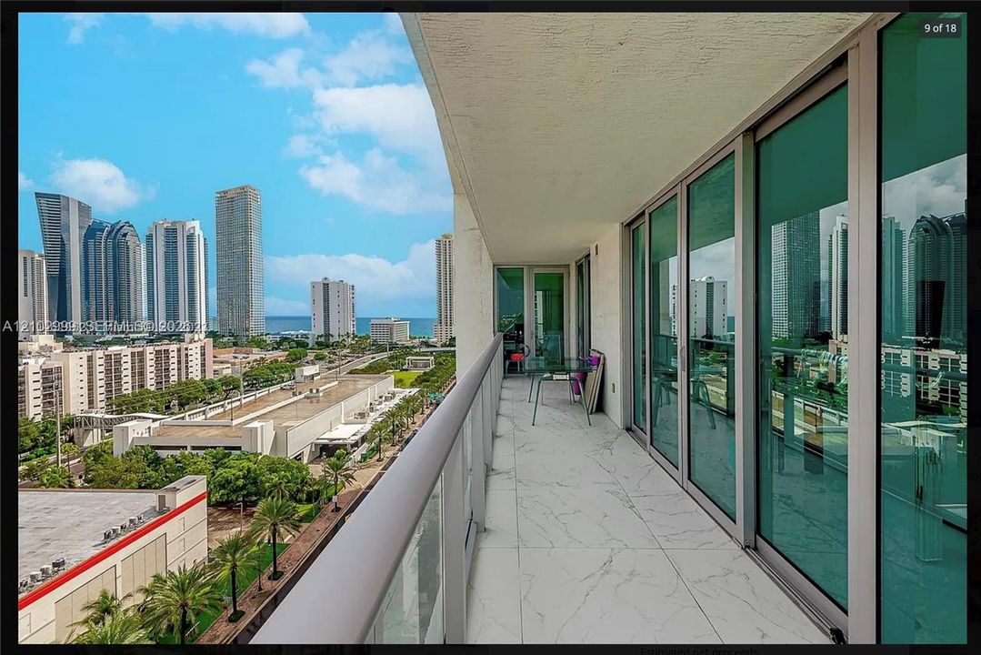 Balcony with a glass and metal railing, large format light-toned tile flooring, and multiple full-height sliding glass doors