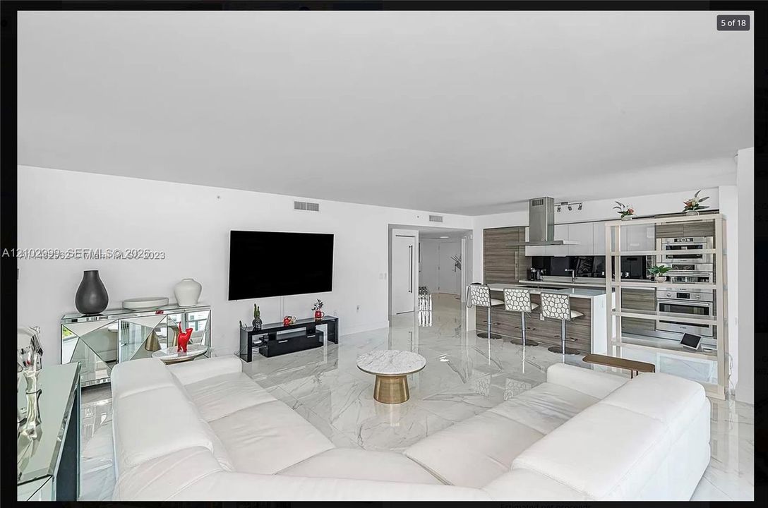 Open-concept living space featuring high ceilings, large-format polished tile flooring, a contemporary kitchen island with seating, stainless steel range hood, and integrated stainless steel appliances