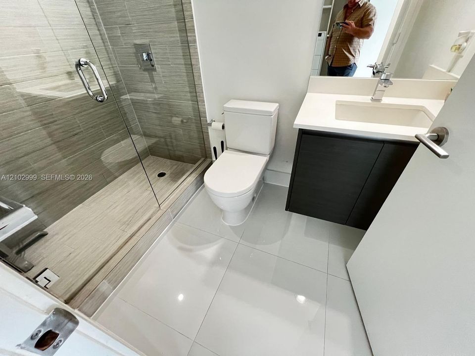 Bathroom featuring large-format tile flooring, a glass-enclosed shower with horizontal wall tile, dark-finish cabinetry, and a white countertop with an integrated sink