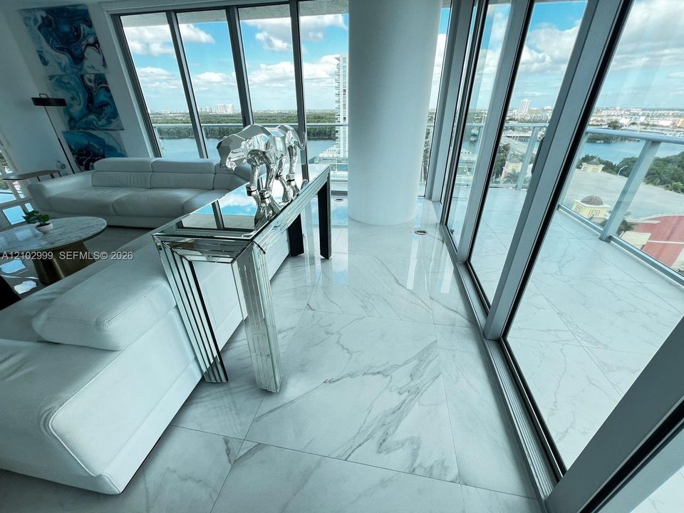 Floor-to-ceiling glass windows, polished large-format tile flooring, and expansive wrap-around balcony with glass railings