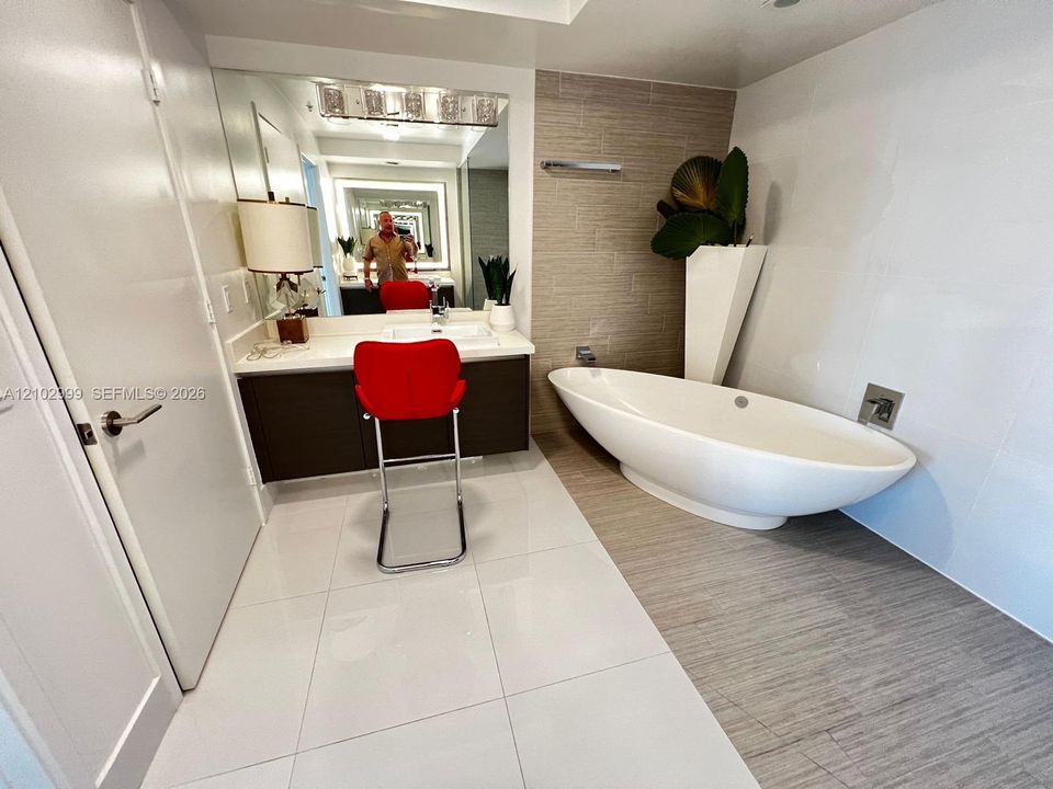 Oval freestanding soaking tub with wall-mounted faucet, floating vanity featuring a rectangular integrated sink, large-format tile flooring, and textured tile accent wall