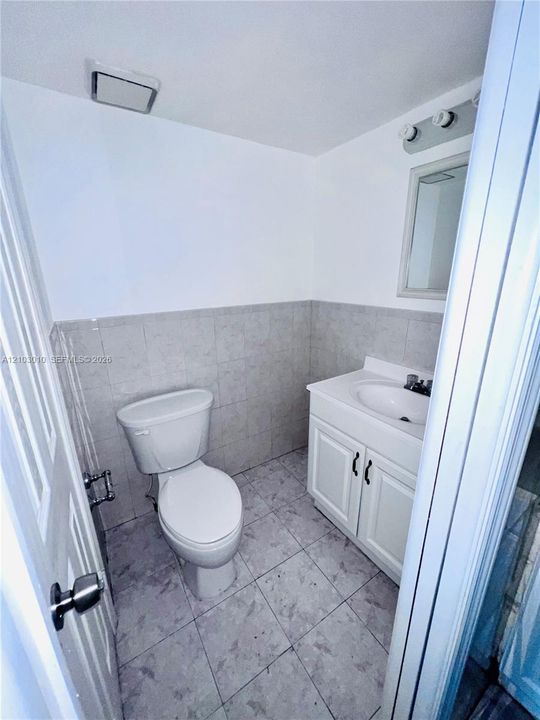 Bathroom featuring a vanity with integrated sink, tile flooring, wall-mounted mirror, and half-height wall tiling