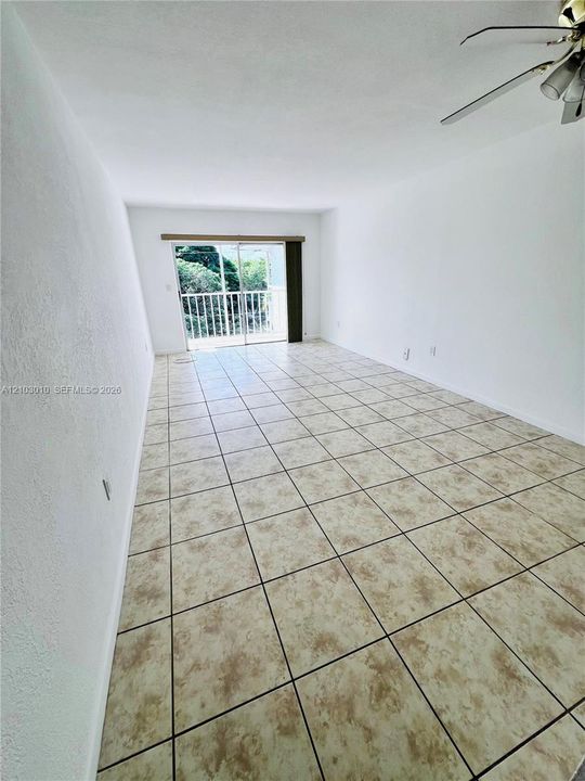 Interior space featuring neutral tile flooring, a sliding glass door, an attached ceiling fan, and a metal balcony railing