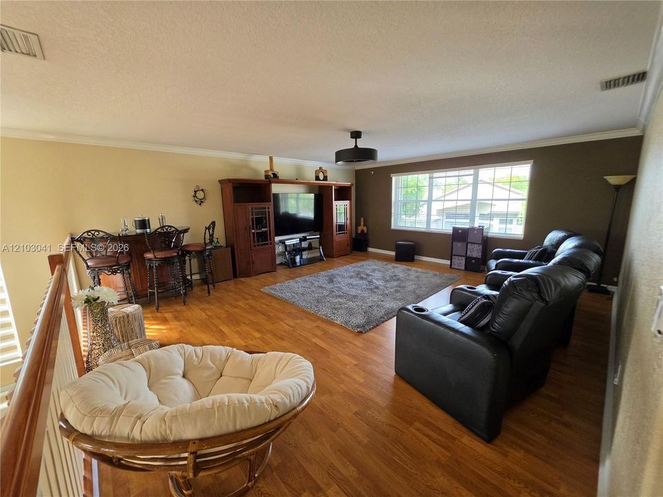 Wood-finish flooring throughout, ceiling fan with integrated lighting, multiple windows providing natural light, and a built-in wet bar with seating