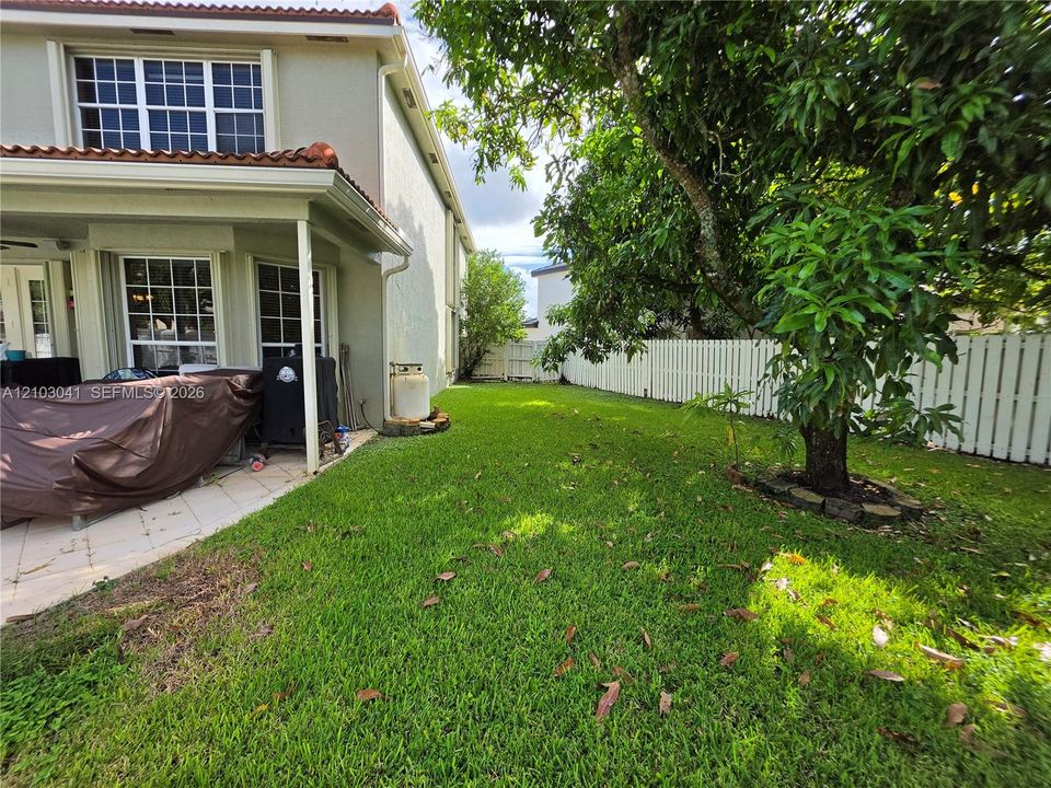 Expansive green space featuring a white picket fence, mature trees, and a covered patio with tiled flooring