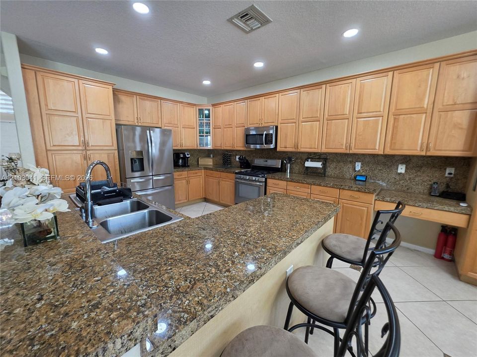 Kitchen featuring extensive light wood-finish cabinetry, stainless steel appliances, granite countertops, and recessed lighting