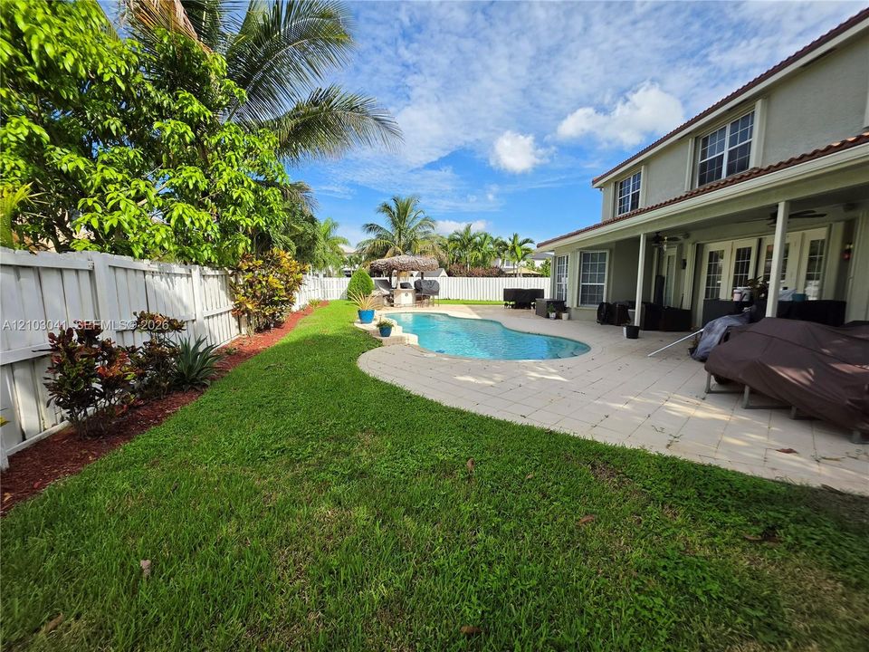 Expansive backyard featuring a manicured lawn, a white privacy fence, and mature trees