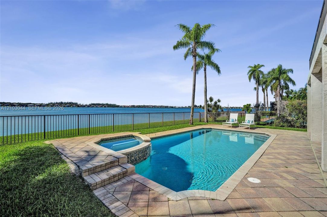Inground swimming pool with integrated spa, stone-paver decking, and metal perimeter fencing overlooking the water