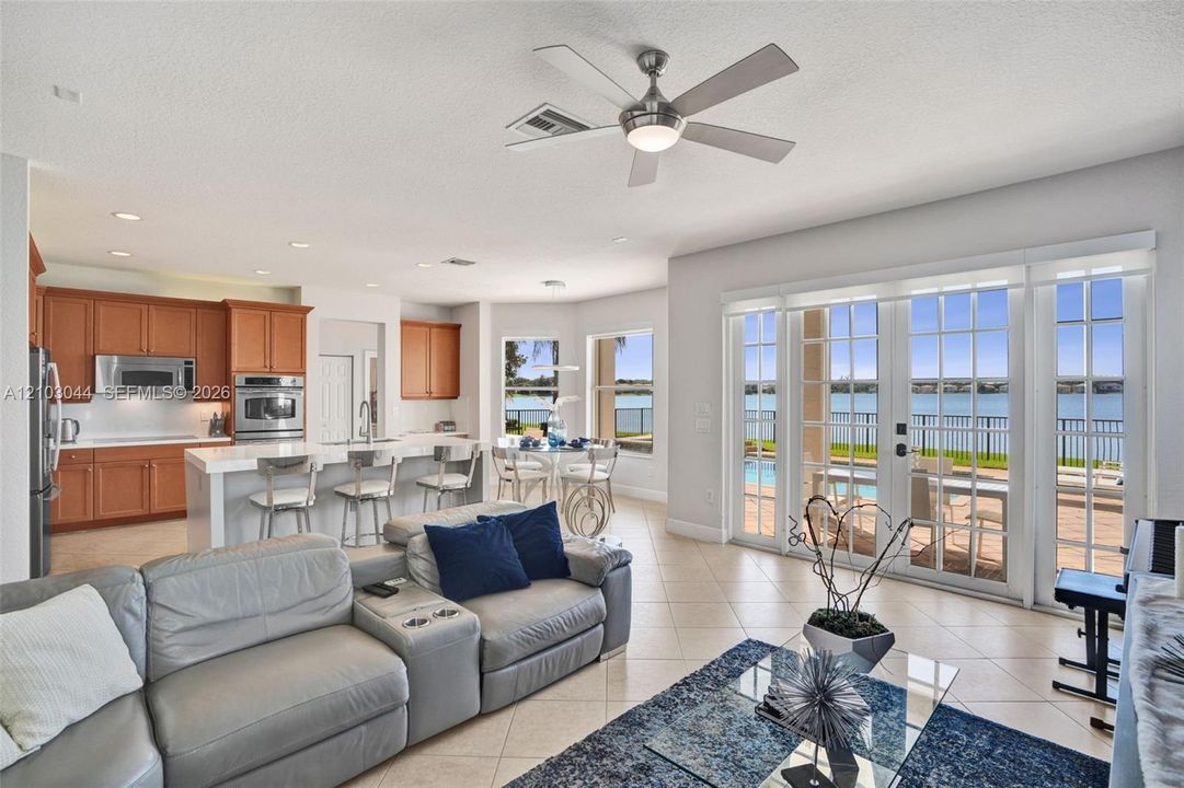 Open-concept living space featuring wood-finish cabinetry, a waterfall-edge center island with a built-in sink, recessed lighting, a modern ceiling fan, and sliding glass doors with exterior patio access