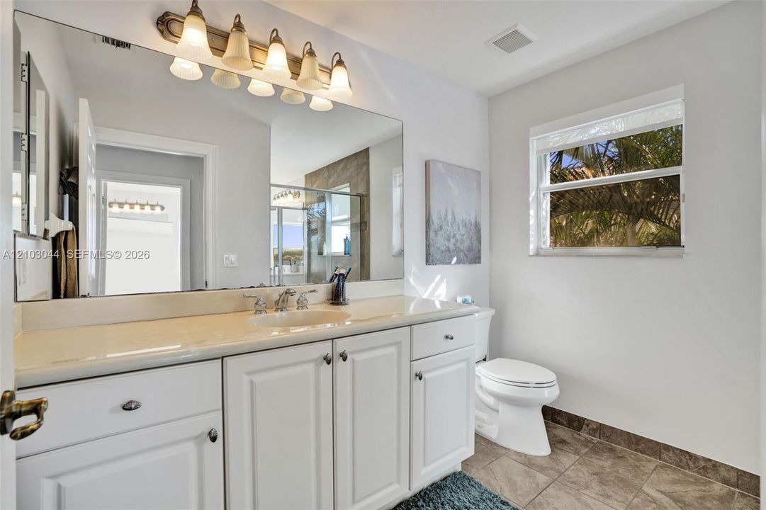 Bathroom featuring a white vanity with integrated basin, expansive wall-mounted mirror, five-light overhead fixture, and tile flooring