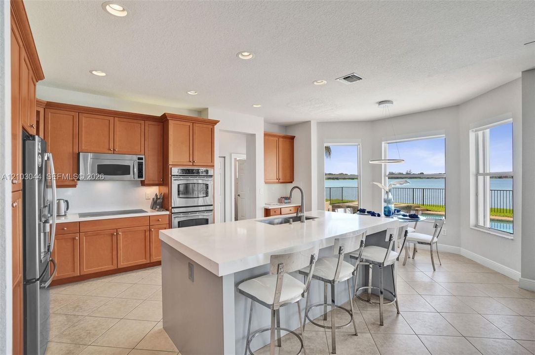 Kitchen featuring shaker-style cabinetry, quartz countertops, a central island with an integrated sink, built-in stainless steel double ovens, and water-facing windows