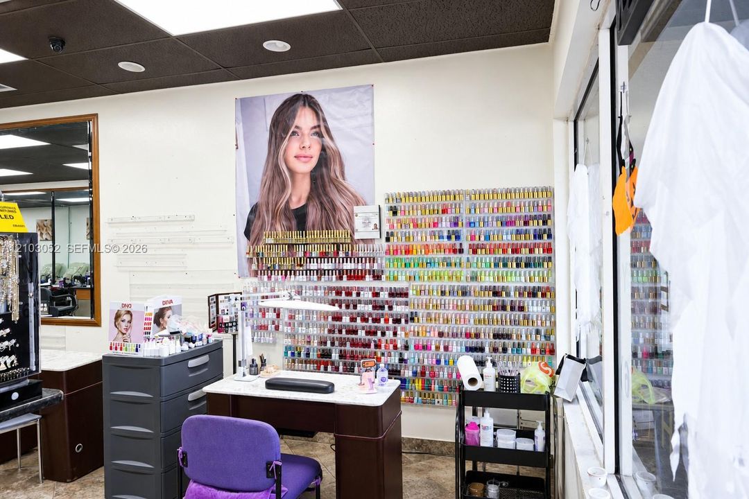 Professional station featuring a built-in manicure desk with stone-finish countertop, wall-mounted display shelving, large-format mirror, and grid-patterned ceiling tiles with recessed lighting
