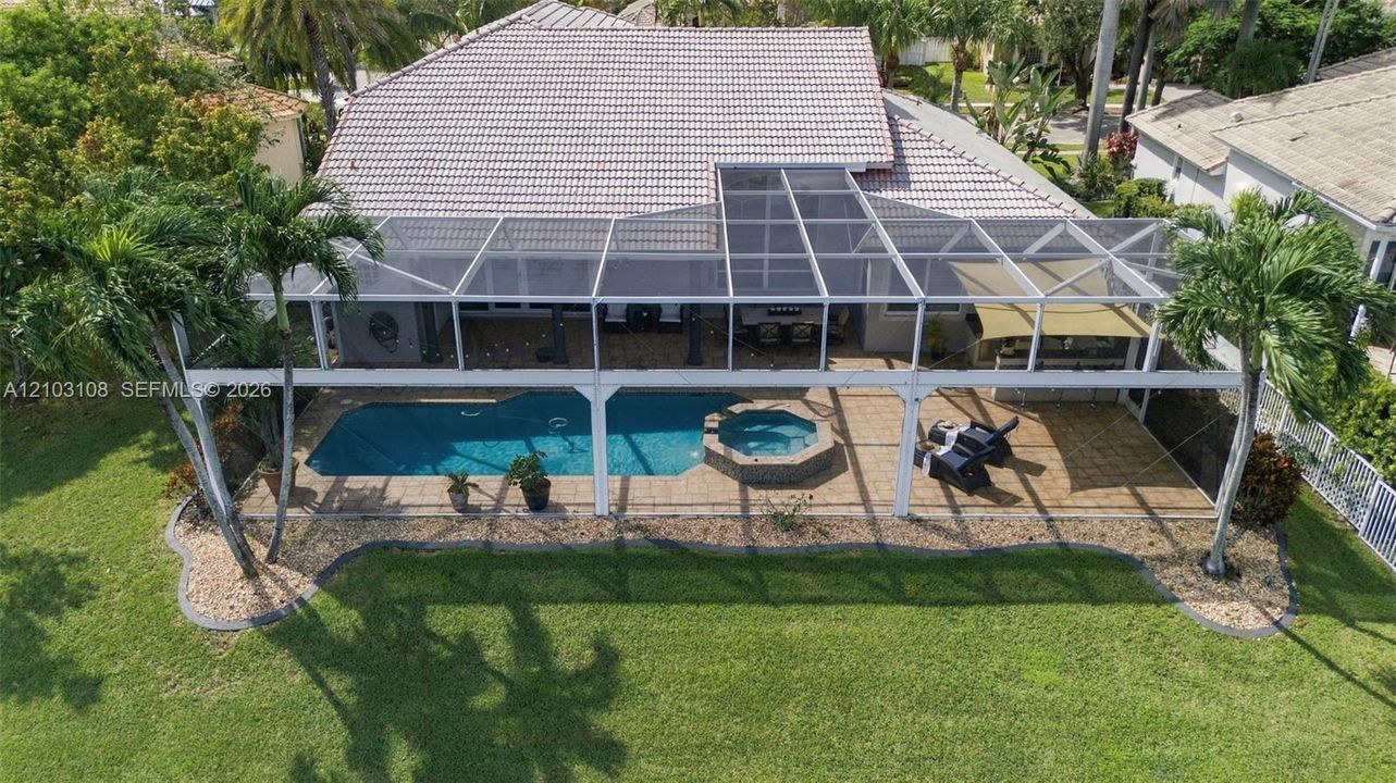 Expansive backyard oasis featuring a resort-style pool with spa, covered lanai with integrated solar panels, mature landscaping with lush lawn, and mature trees providing natural shade