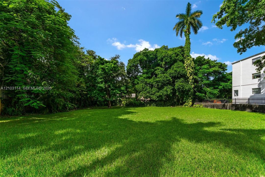 Expansive grass lawn featuring mature trees, a tall palm tree, and stone masonry perimeter walling