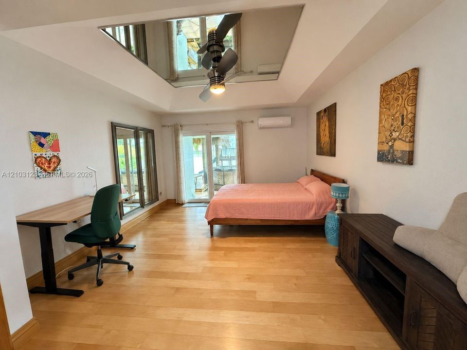 Tray ceiling featuring a central mirrored panel and integrated ceiling fan, wood-finish flooring, and sliding glass patio door