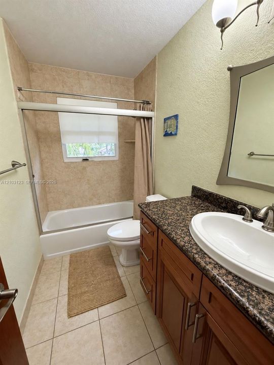 Bathroom featuring a wood vanity with stone countertop, drop-in sink, shower-tub combination with tile surround, and tile flooring